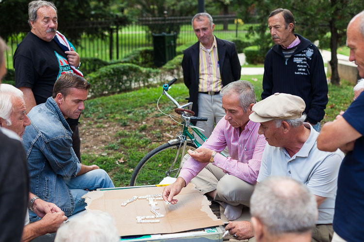 A group of old men are playing several rounds of dominos in a park downtown. 