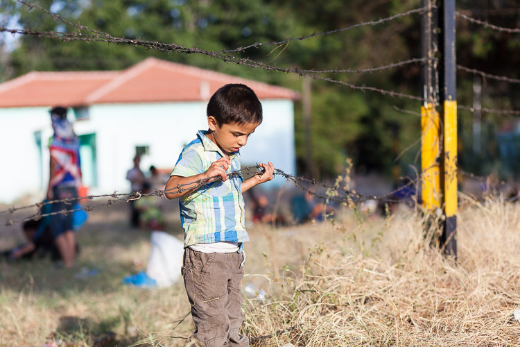 A young boy near the Idomeni train station looks at a piece of barbed wire. While travelling the Balkan route towards the EU, he will often be confronted with similar defenses.