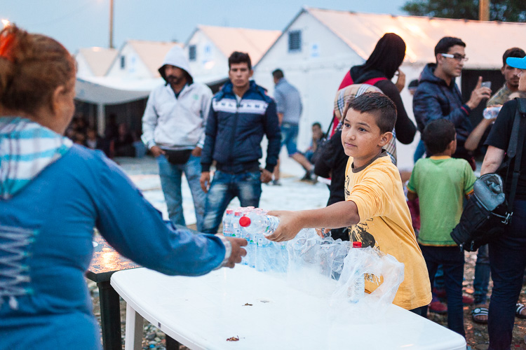 A young (refugee) boy hands out water to other refugees inside the Gevgelija refugee camp.