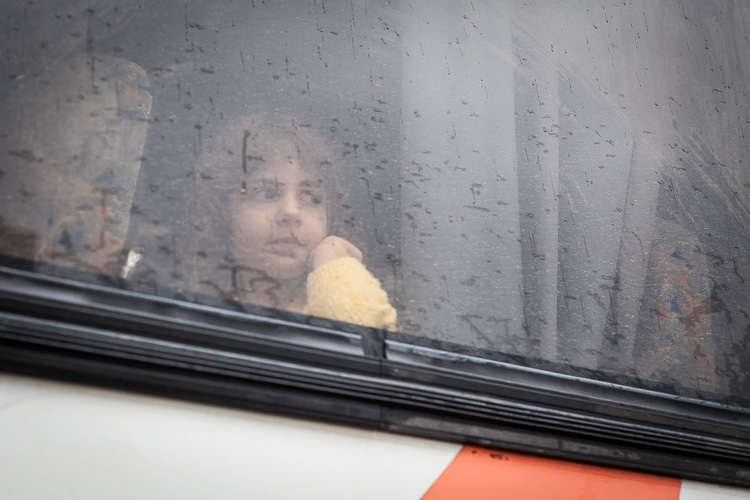 A young girls stares out the window of a bus, as it is pouring down outside the Gevgelija refugee camp.