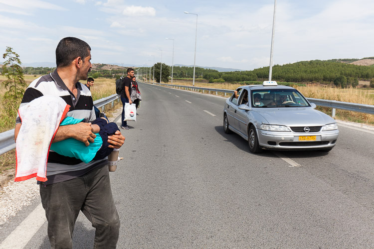 A father in distress, carrying his disabled child while attempting to take a taxi on his way to Idomeni, Greece